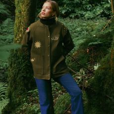 A model wearing a green jacket with a nature design standing in the woods