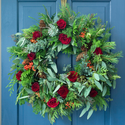 Wreath adorned with roses, berries, and pinecones on a blue door.