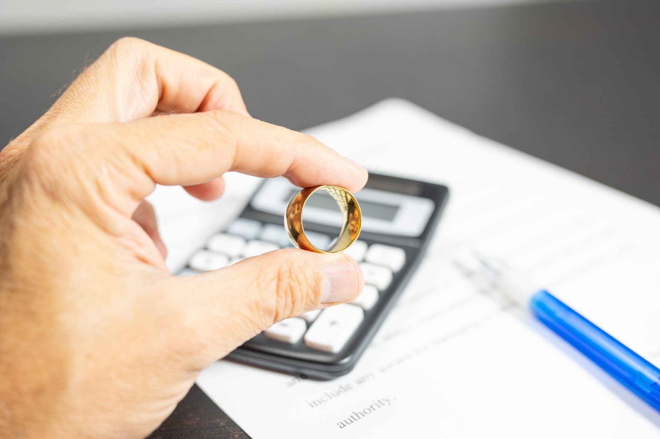 A man holds a golden boot wedding ring. On the table is a calculator and a pen