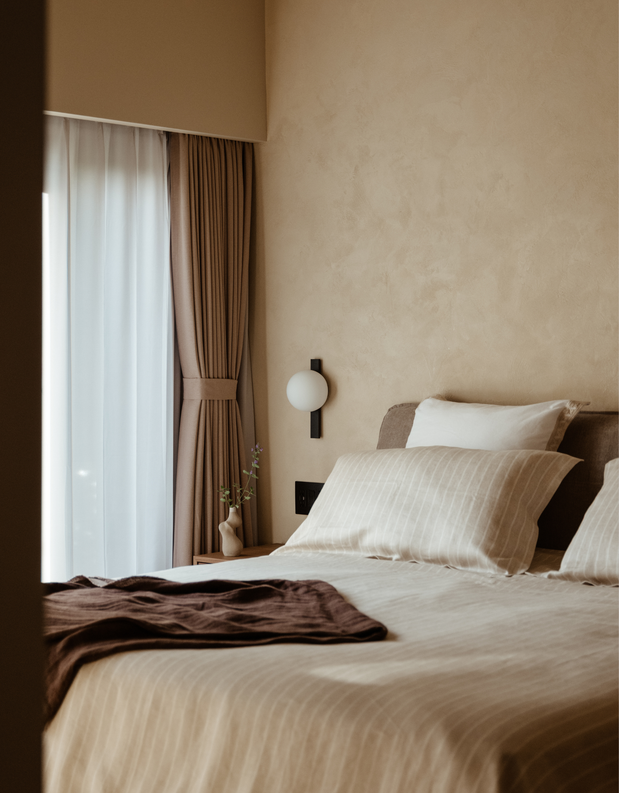 A minimalist living room with a striped beige bedspread, a brown throw, a mini vase, and brown curtains