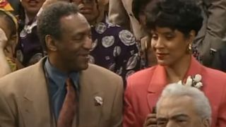 Bill Cosby looks over smiling at Phylicia Rashad while sitting on bleachers in The Cosby Show series finale.