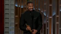 Michael B. Jordan smiling while talking into a mic and holding his Oscar. 