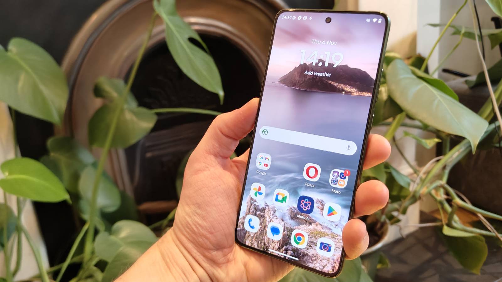 The Motorola Edge 70&#039;s home screen, while the phone is being held in a hand.