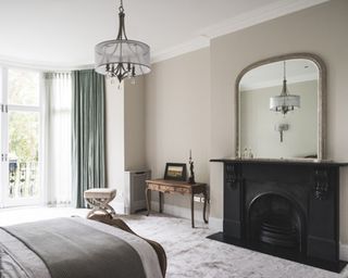 Black fireplace in bedroom with large framed mirror on mantelpiece, pendant ceiling light and green curtains with grey carpet by Renaissance London