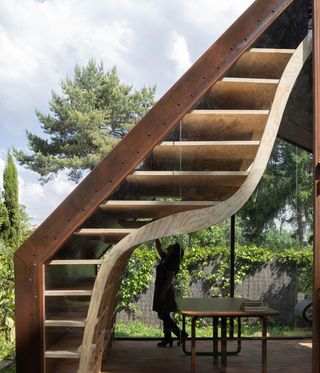 A curving wooden bookcase against glass window