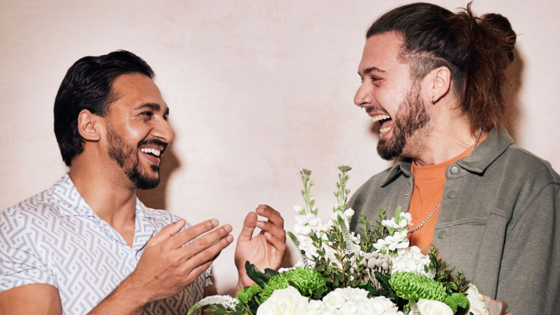 an image of two men laughing and holding a bouquet of flowers