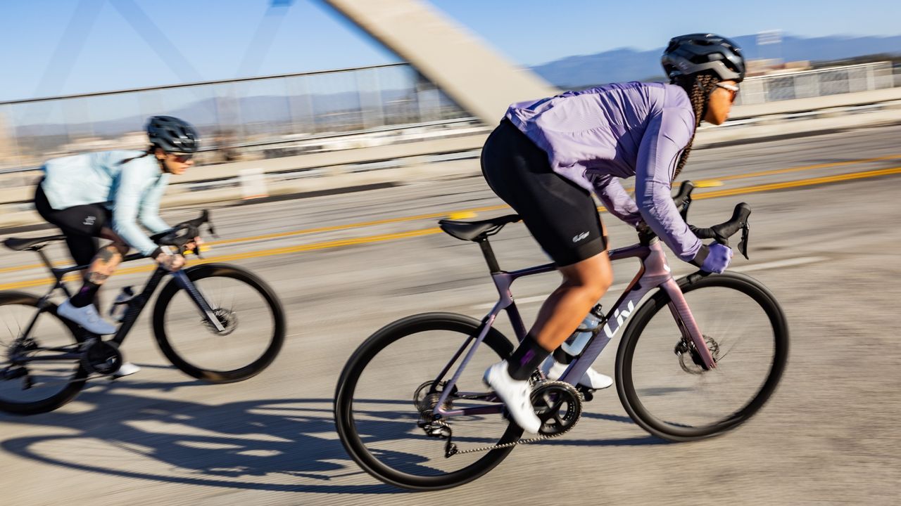 The rider in the image is out of the saddle riding a Liv EnviLiv bike in purple with a matching purple jacket 