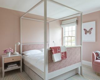 A girls bedroom with pink walls, white four poster bed and Damien Hirst pink butterfly artwork