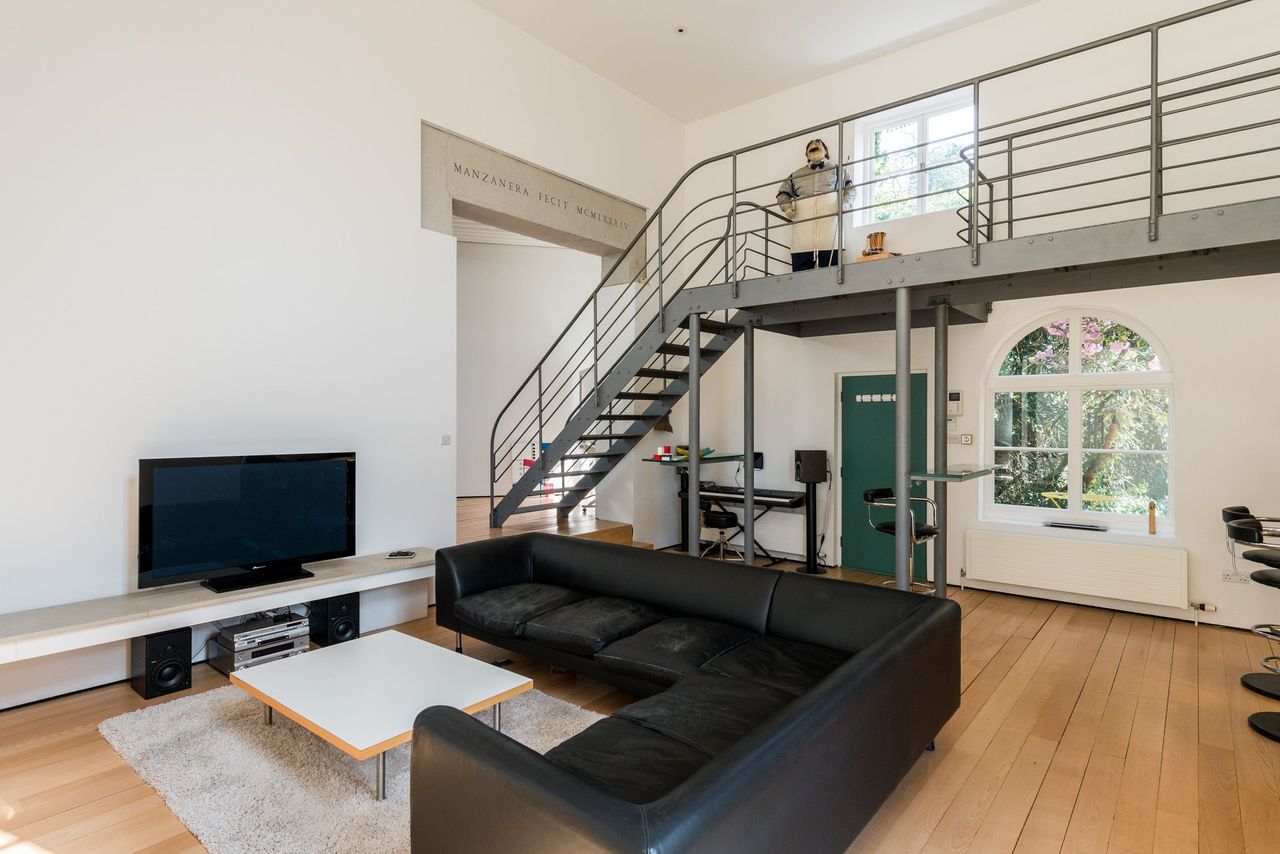 The living room has a staircase and a black sofa and tv with wooden flooring