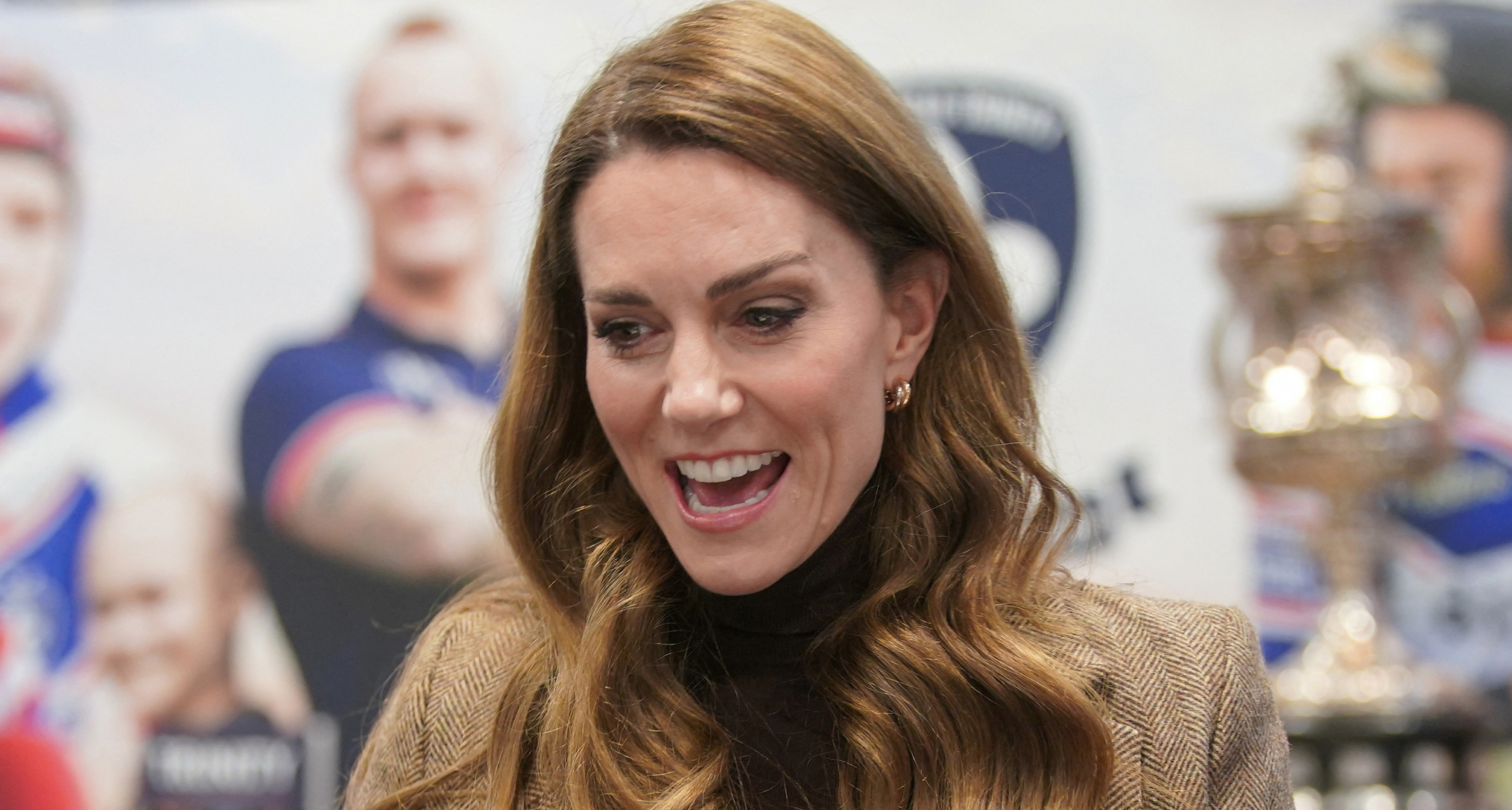 Kate Middleton laughing wearing a brown blazer