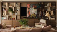 living room with wood joinery and white armchair and art half covering a TV in the joinery