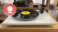 A photograph of a white Rega Planar 2 on a wooden hi-fi rack