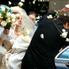 Angry Sarah Jessica Parker in wedding gown hitting groom with flower bouquet