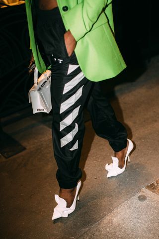 A guest at Paris Fashion Week wearing Off-White black and white striped track pants, a green blazer, and sculptural white pumps