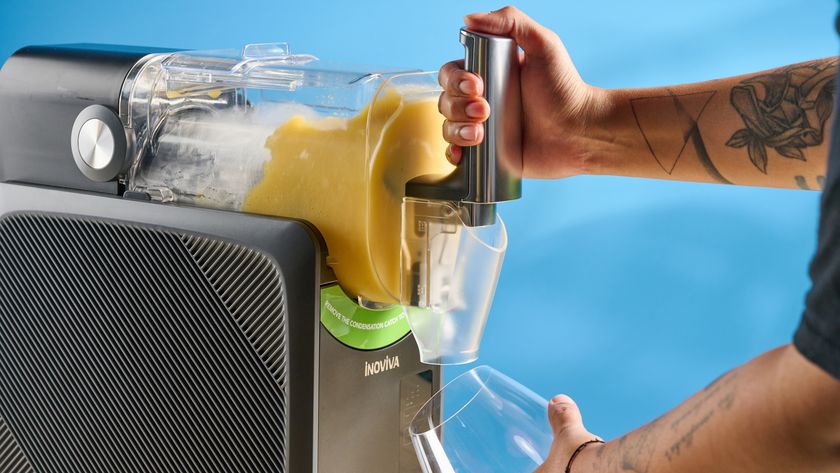 the inoviva slushie machine, a slushie maker with a plastic cylinder body, a dispensing spout, photographed making orange juice slush against a blue tom&#039;s guide background