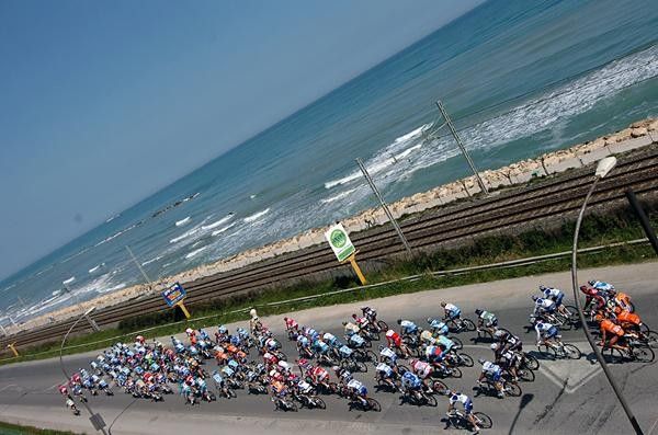The peloton rolls along the beach front, seperated by the railway line.