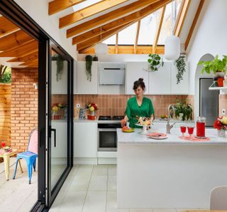 Woman in a white kitchen extension with terracotta metro subway tiles, kitchen island and sliding doors