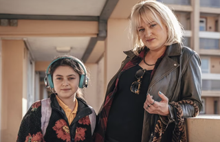 Fleur Tashjian wearing headphones standing next to Daisy May Cooper, who is holding a handbag