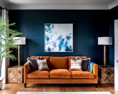 A burnt orange velvet couch for a small living room with dark blue walls and abstract art.