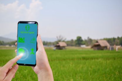 Person In A Field Holding A Phone With A Gardening App Open