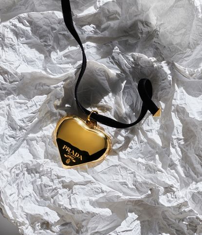 Prada gold heart on black necklace, resting on crumpled paper
