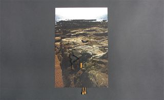 View of the other side of Givenchy’s invitation pictured against a grey background. This side features a shot of a rocky beach and a cut out of a woman's face