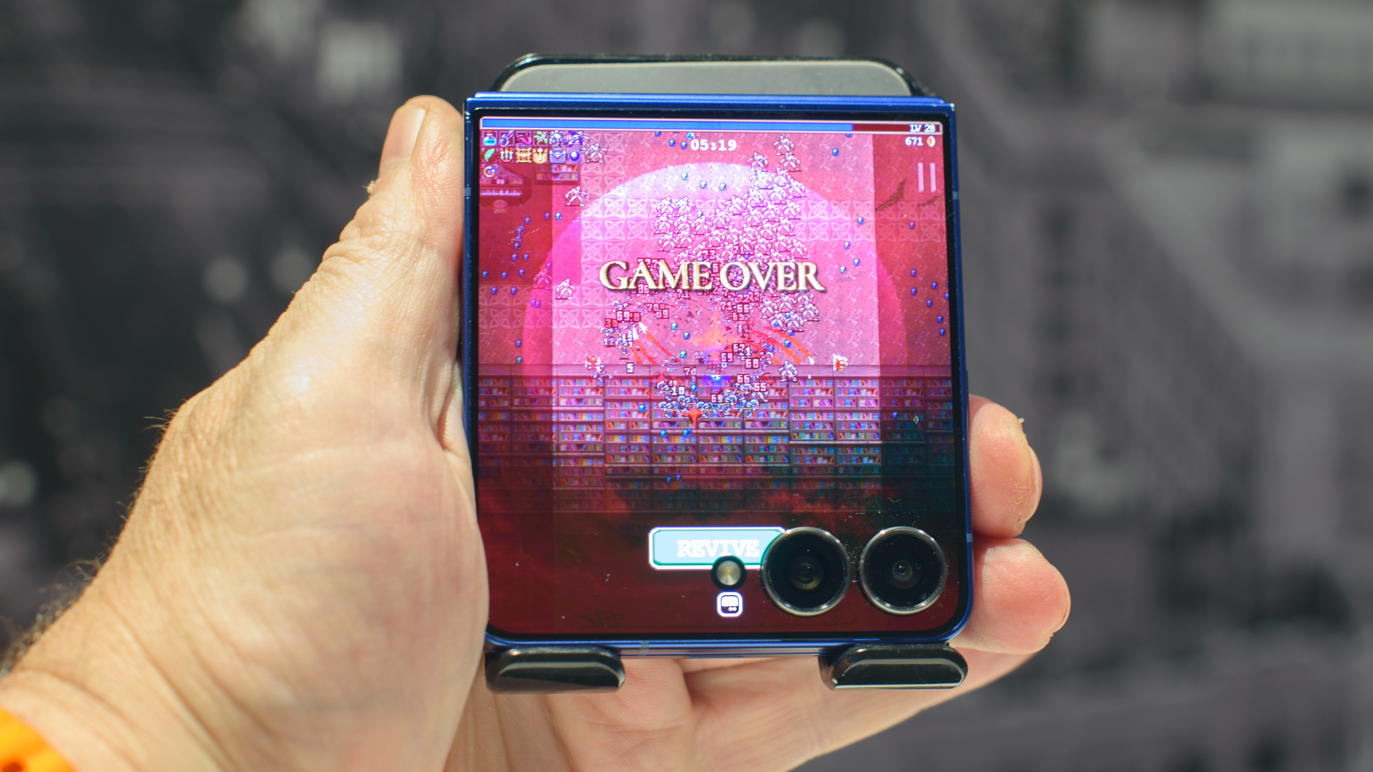 Samsung Galaxy Z Flip 7 in blue in hand showing Vampire Survivors Game Over screen