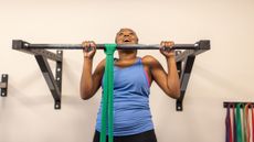 Woman performing pull-up using green resistance band for assistance. She looks elated to have her chin reach the bar