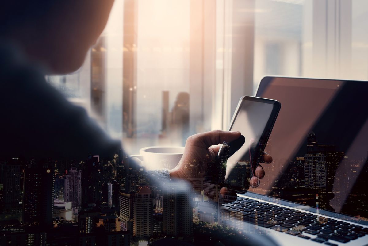 Man holding mobile phone over laptop with double exposure city overlay