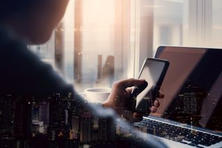 Man holding mobile phone over laptop with double exposure city overlay