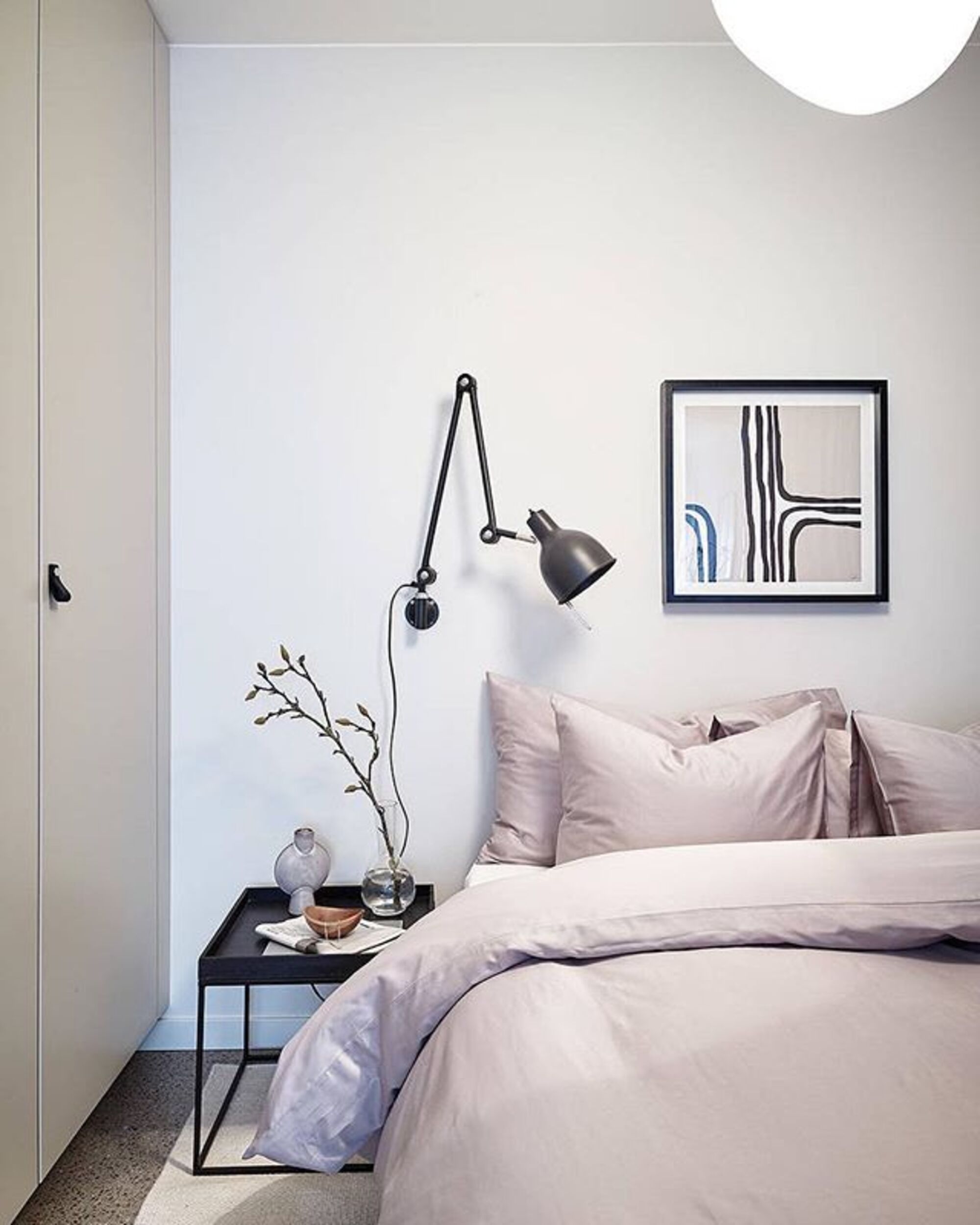 A bedroom with plump, light pink bedding and a anglepoise-style lamp fixed to the wall