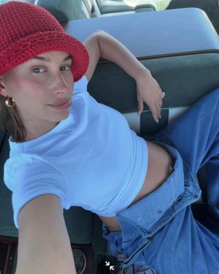 Hailey wears a red crochet hat, white joe's jeans baby tee, and denim overalls.