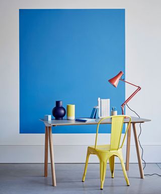 Blue color block on wall to zone home office set-up with yellow metal chair and small desk
