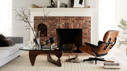 Black Friday furniture sales. Living room with eames lounge chair in dark wood and black leather, large brick fireplace, glass and wood coffee table, cream carpet 
