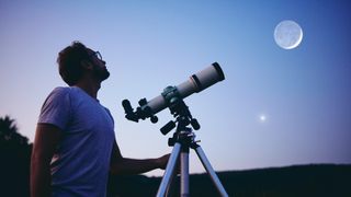 Telescope deals and discounts: Image shows man next to telescope looking at moon