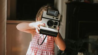 Best instant camera: a young girl holding a vintage instant camera over her face to take a photograph