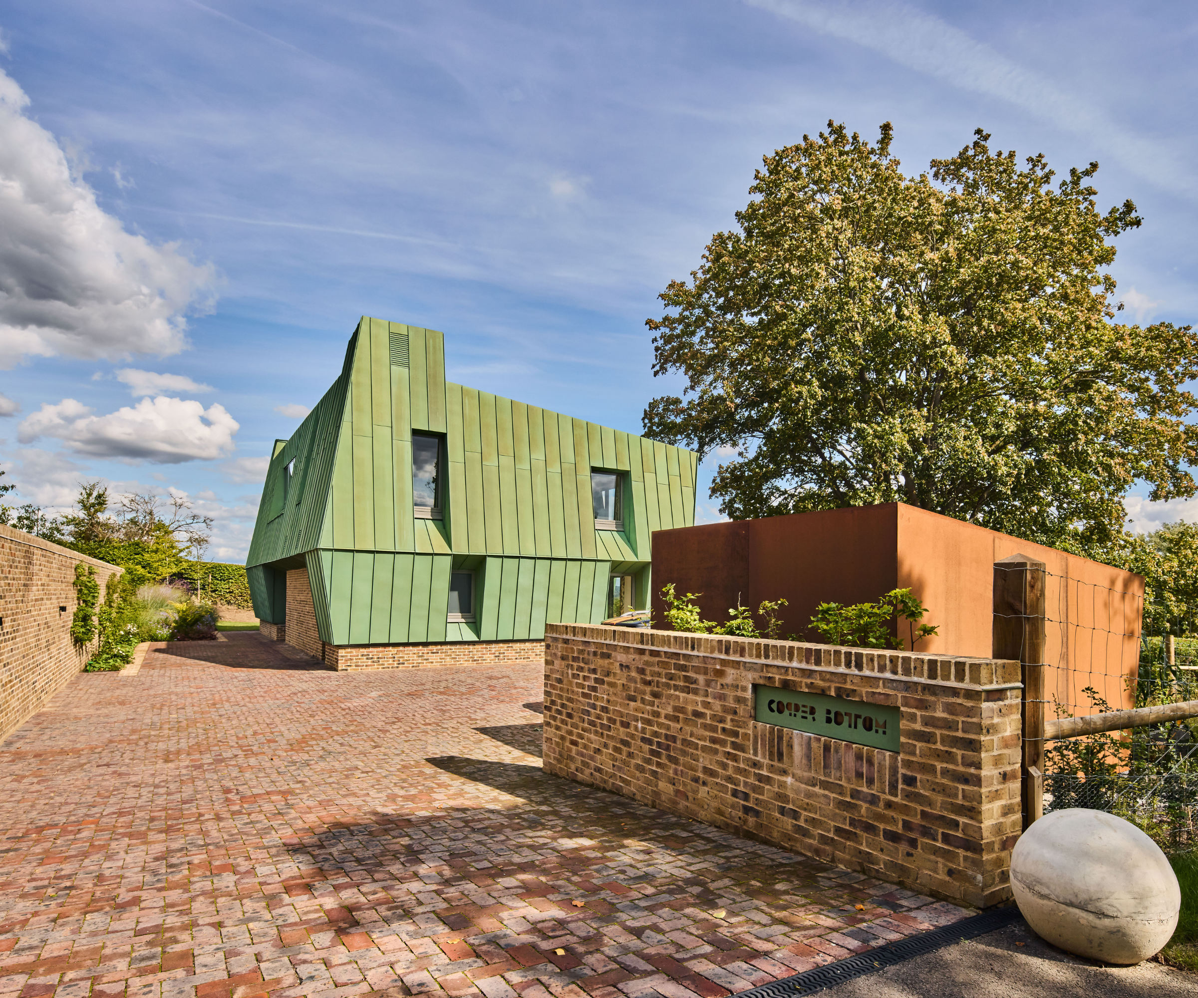 Brick driveway leading up to a green house with a tree on the right hand side