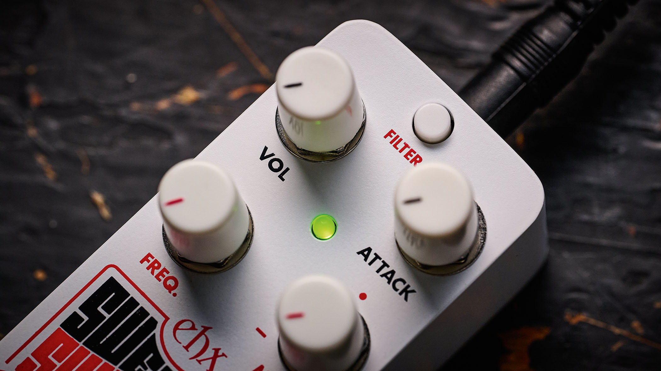 Electro-Harmonix Pico Swello: the compact mini-pedal is finished in white and has black and white text, four knobs, and is photographed against a distressed wood floor.