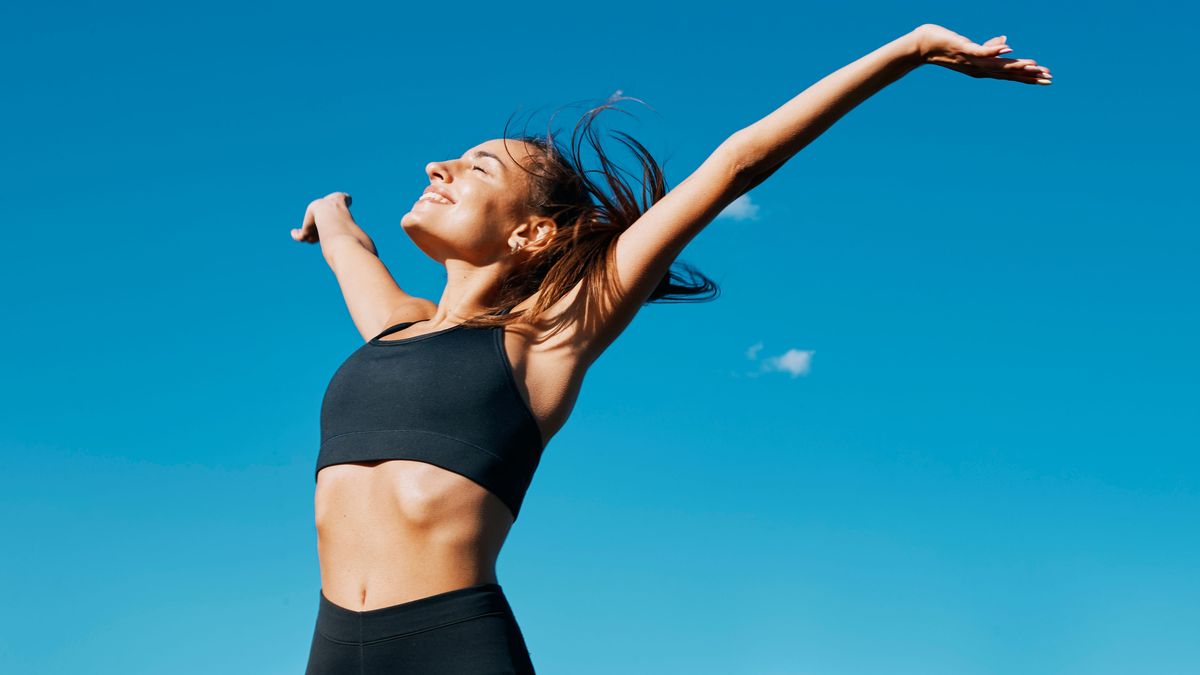 a photo of a woman wearing gym kit standing in front of a blue sky