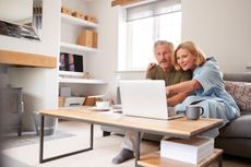 2A8D3PA Senior Couple Sitting On Sofa In Lounge At Home Using Laptop Together