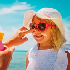 best sunscreen for children - image of a small girl wearing sunglasses and a sun hat having sun cream applied to her face