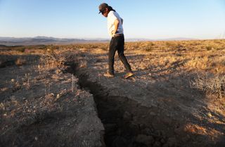 a man surveys a crack in the earth from the ridgecrest quake