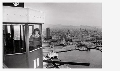Old black and white photograph of young girl looking out of cable car with a European city landscape behind her.