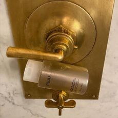 A Ouai shampoo bottle in a gold and marble shower