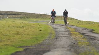 Two gravel riders riding a rough tarmac track