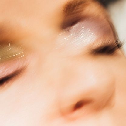 Closeup of a woman wearing glitter eyeshadow and tubing mascara. Young woman has her eyes closed and long eyelashes. 