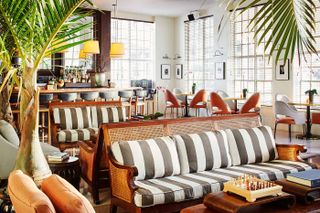 The laid-back, modern rustic meets mid-century modern design interiors of a hotel lobby feature woody and upholstered furniture in a lofty enviornment.