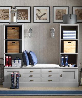 Grey bench storage unit with blue pillows and picture frames and flights against the wall