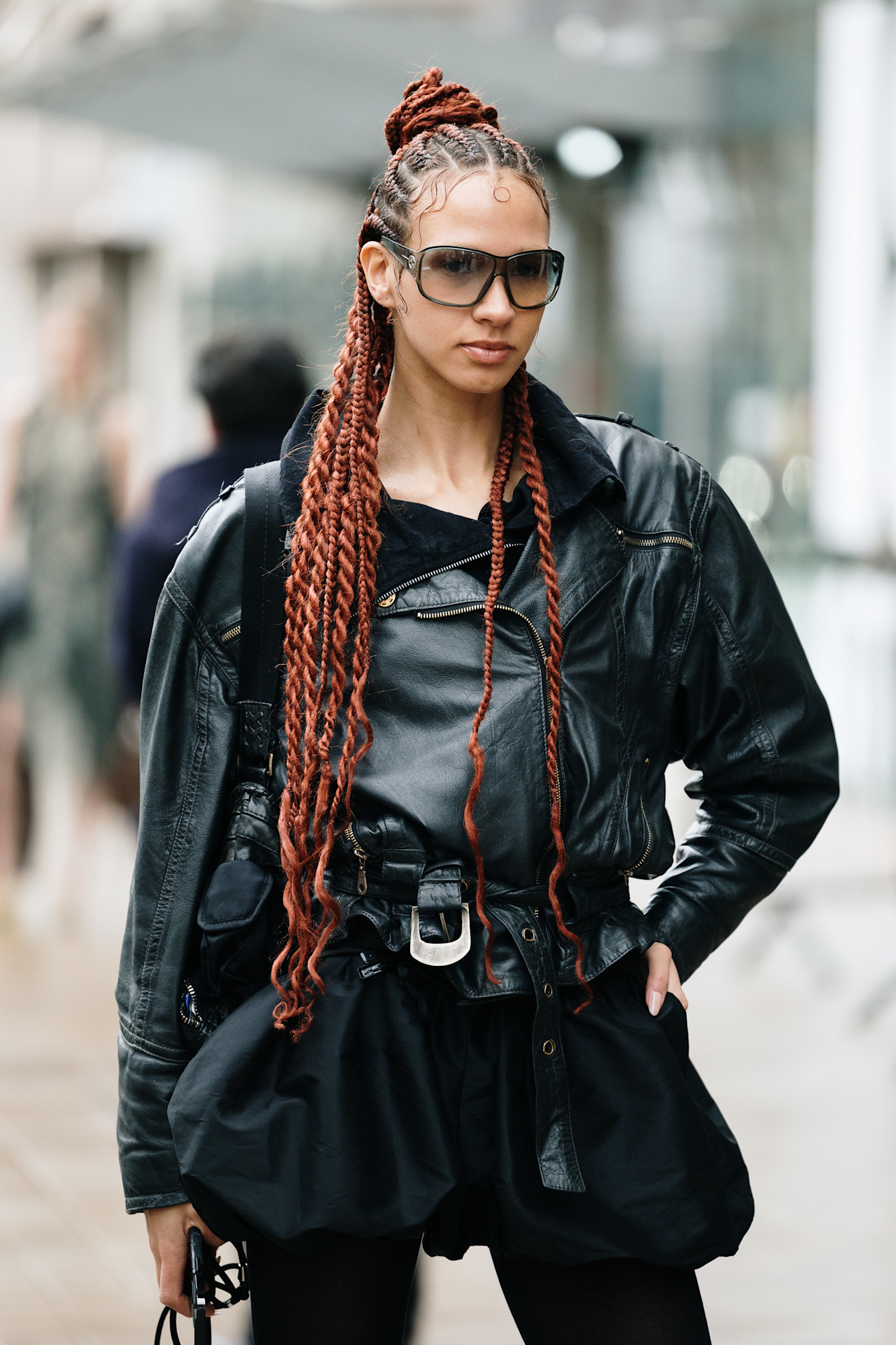 A woman with long copper coloured braids and twists, worn in a half-up, half-down hairstyle with a bun