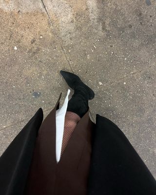 A pair of suede Jimmy Choo stiletto boots paired with fishnet tights, a brown skirt, and a black coat.